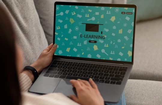 Persona usando una laptop con una pantalla de e-learning, mostrando un diseño educativo con iconos de aprendizaje y un birrete de graduación